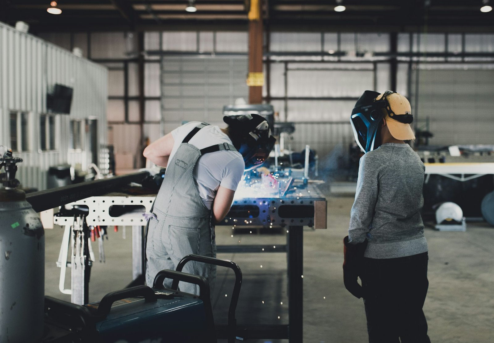 A female welder teaches a child how to weld in a workshop