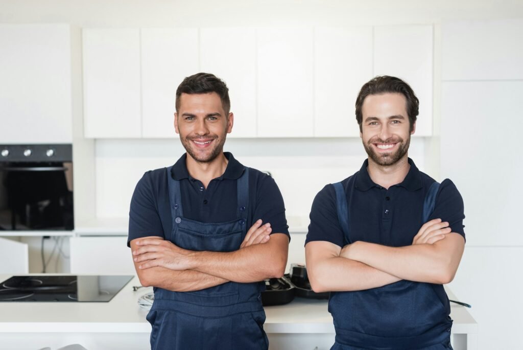 happy handymen in uniform standing with crossed arms in kitchen