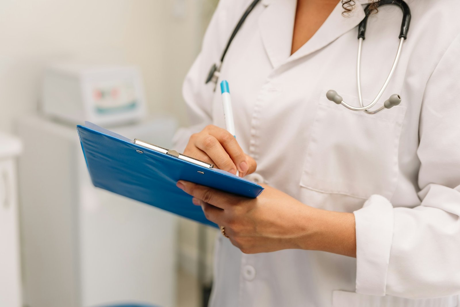 unrecognizable female doctor filling up medical form at clipboard